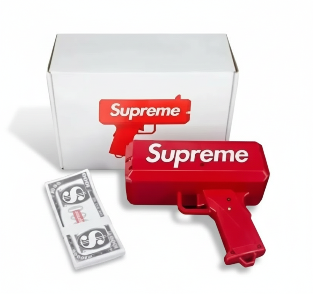 A red plastic money gun with the word 'Supreme' printed on it, alongside a box marked with the same brand and a stack of fake dollar bills.