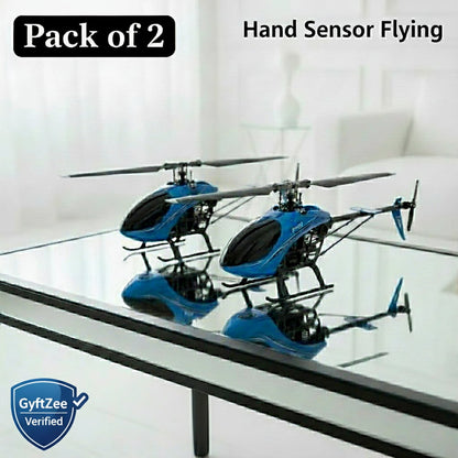 Two blue and black toy helicopters on a glass table with 'Pack of 2' and 'Hand Sensor Flying' text above.