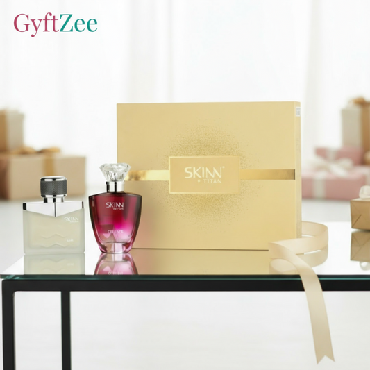 Two perfume bottles and a gold box with 'SKINN' branding on a reflective surface.